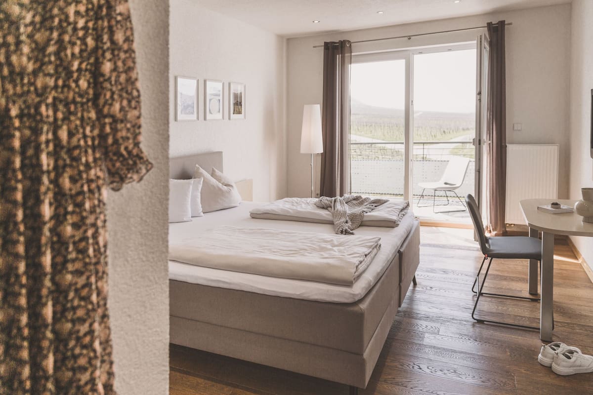 A hotel room with a bed, a desk, a chair, and a view of the outdoors.