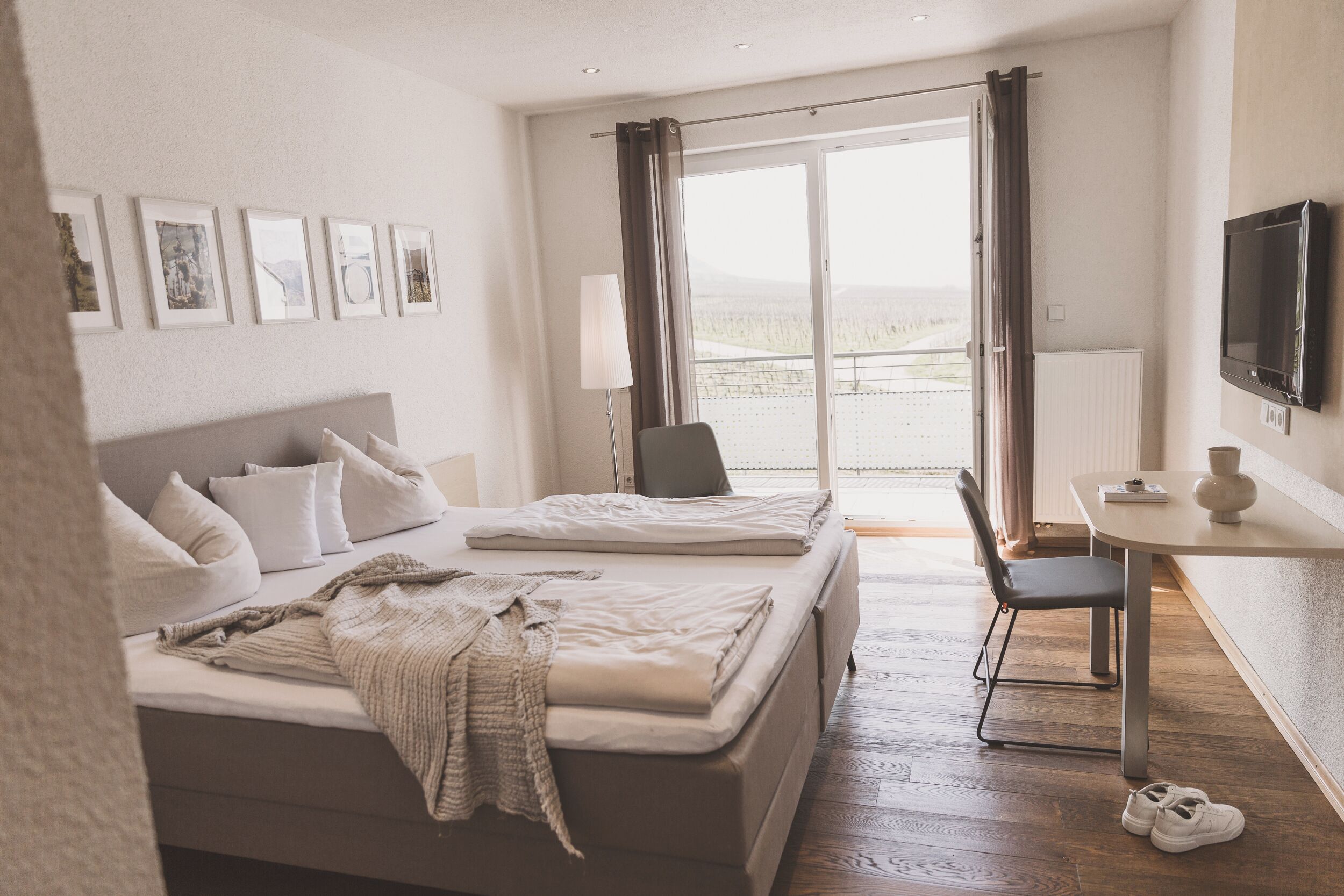 A hotel room with two beds, a desk, a chair, a TV, and a balcony with a view.