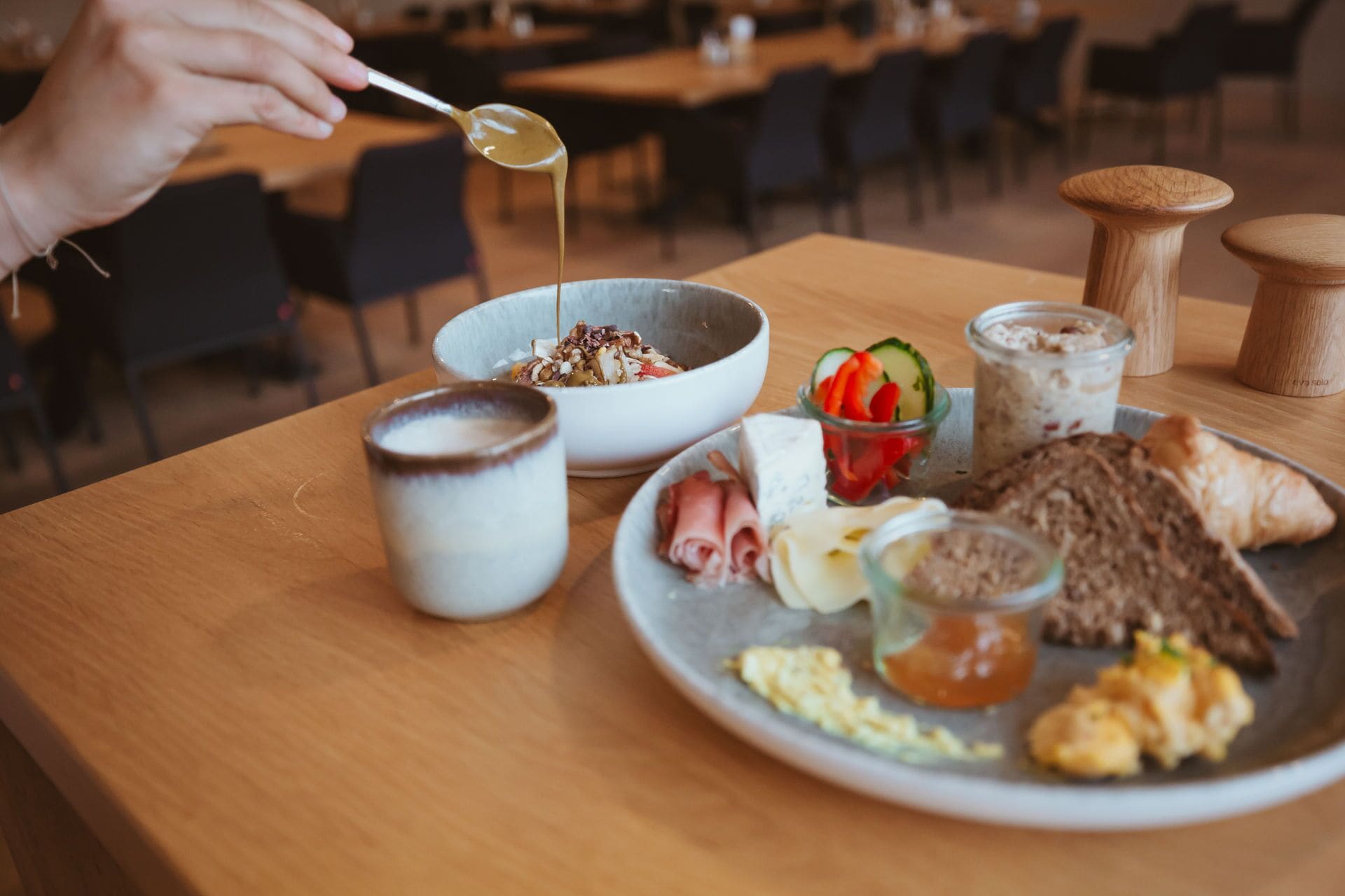 A breakfast setting with a variety of food items on a table, including a bowl of cereal, a plate with eggs, toast, and a small dish of jam.