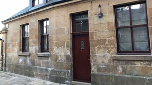 Un bâtiment en pierre avec une porte de couleur brun foncé, une fenêtre ornée de vitraux et une cheminée.