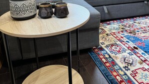 Un salon avec un canapé gris, une table ronde en bois agrémentée d’objets décoratifs, une plante en pot et un tapis à motifs.