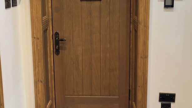 Une porte en bois ornée d’un panneau de verre décoratif, un thermostat fixé au mur et un interrupteur.