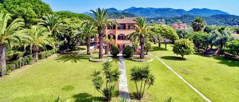 A large, multi-story building with a central courtyard surrounded by palm trees and well-maintained lawns.