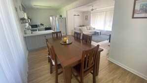 Un comedor con mesa y sillas de madera, una cocina al fondo y una sala de estar con sofá y mesa baja.