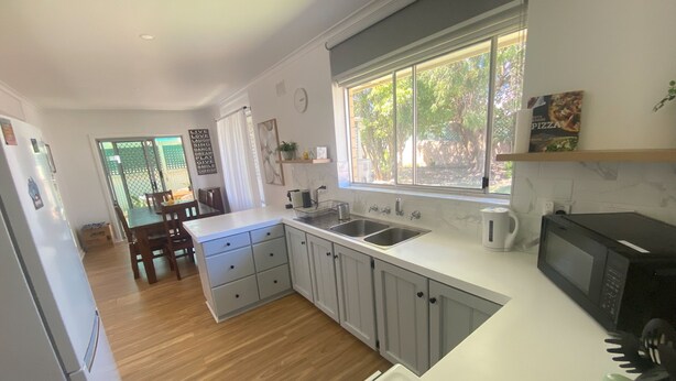 Una cocina moderna con armarios blancos, un lavamanos doble y un ventanal con vistas a un jardín.
