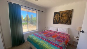 Un dormitorio con una cama grande, una ventana con cortinas, un cuadro en la pared y una lámpara de noche.