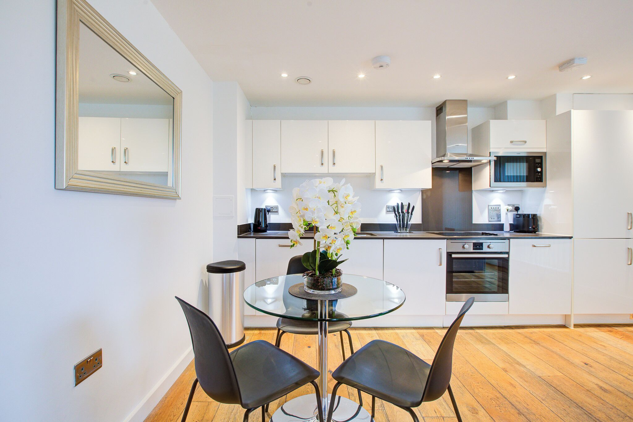 A modern kitchen with white cabinets, a glass dining table, and two black chairs.