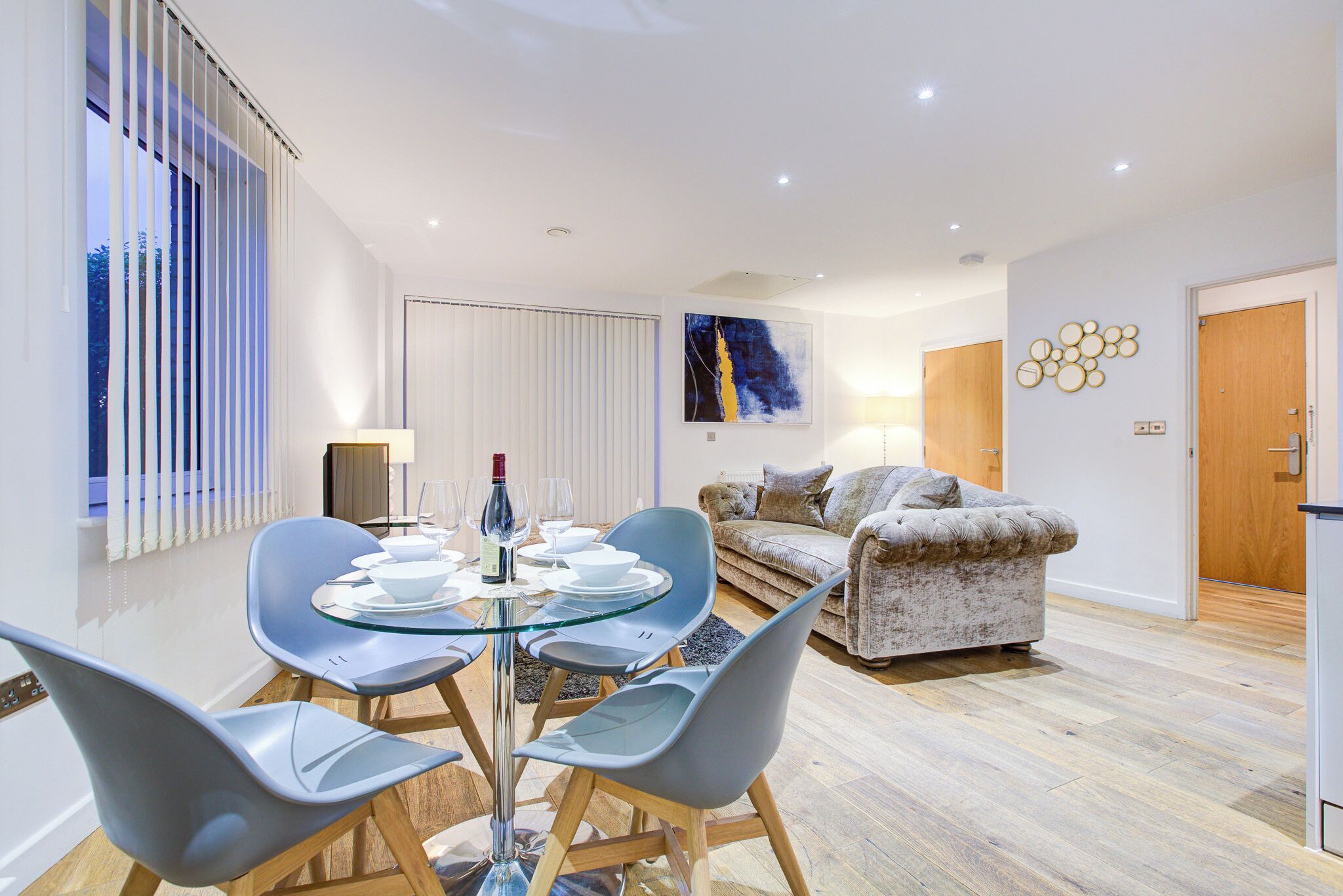 Ein modernes Wohnzimmer mit einem Glastisch, grauen Stühlen, einer Couch und Holzboden.