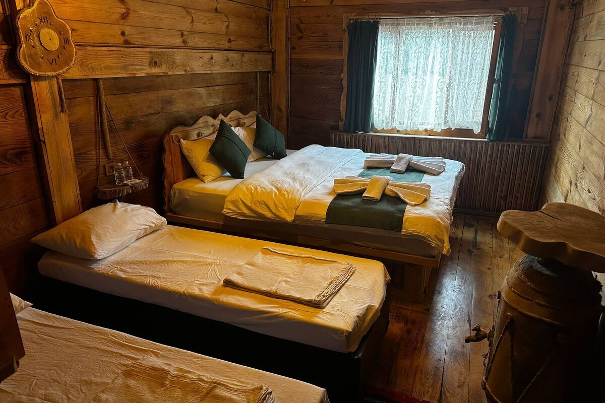 Une chambre rustique dans un chalet, avec deux lits, une horloge murale en bois, une fenêtre avec des rideaux et un tonneau en bois.