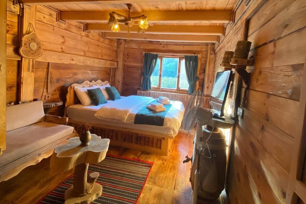 L’intérieur d’un chalet en bois, avec un lit, un canapé, un ventilateur et une fenêtre.