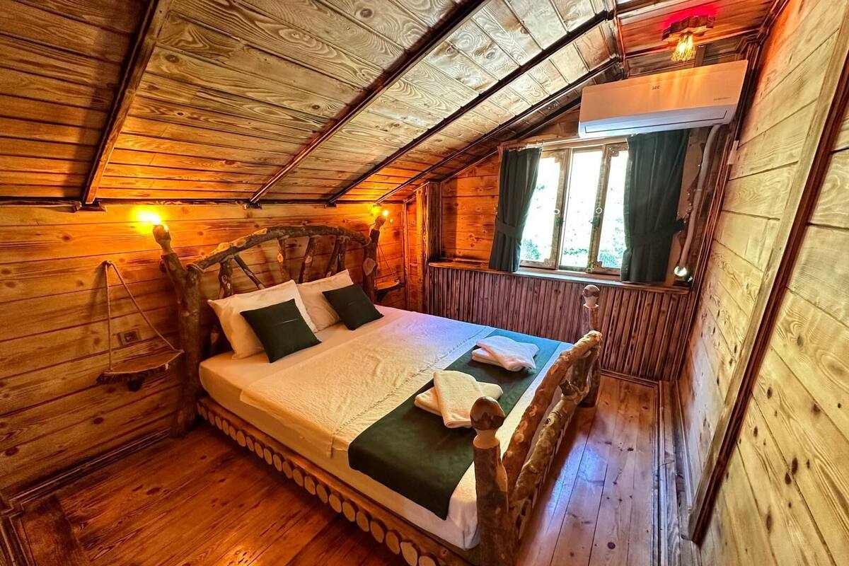 Une chambre dans une cabane en bois, avec un lit, des oreillers et une fenêtre avec des rideaux.