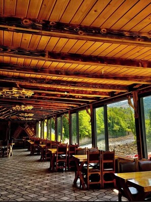 En restaurant med træbjælker i loftet, store vinduer og flisegulv.