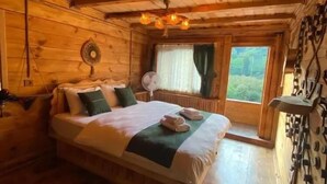 A wooden cabin bedroom with a bed, a fan, and a window with a view. - Rubaşi Butik Otel & Restoran (Findikli)