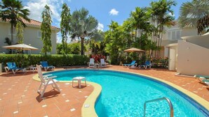 A swimming pool with lounge chairs and umbrellas, surrounded by palm trees and a tiled deck. - Turtle View by Bluescape (Holetown)