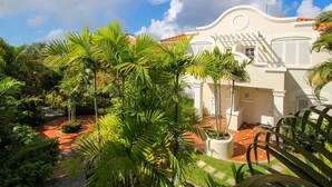 A white building with a curved facade and a red-tiled roof, surrounded by lush greenery and a paved pathway. - Turtle View by Bluescape (Holetown)