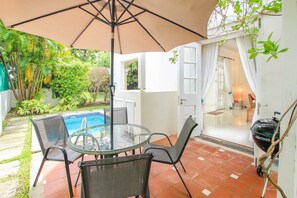 An outdoor patio with a glass table and chairs, a pool, and a covered area with a view of the garden and house interior. - Turtle View by Bluescape (Holetown)