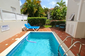 A swimming pool with a caution sign, blue lounge chairs, and a patio area with a table and chairs. - Turtle View by Bluescape (Holetown)