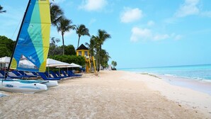 A beach with lounge chairs, a sailboat, and a yellow building. - Turtle View by Bluescape (Holetown)