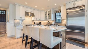 A modern kitchen with white cabinets, stainless steel appliances, and a central island with bar stools. - 916 Empire Skiers Secret 4 Bedroom Home (Park City)