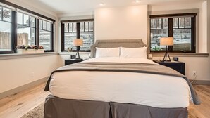 A modern bedroom with a large bed, two bedside tables, and a window with a view of a snowy landscape. - 916 Empire Skiers Secret 4 Bedroom Home (Park City)