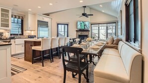 A spacious living area with a dining table set for six, a fireplace, and a large window with a view. - 916 Empire Skiers Secret 4 Bedroom Home (Park City)