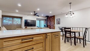A modern kitchen with a large island, wooden cabinets, and a dining area with a round table and chairs.