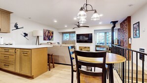 Una cocina moderna con armarios de madera, un comedor con mesa y sillas, y una sala de estar con sofá y televisor.