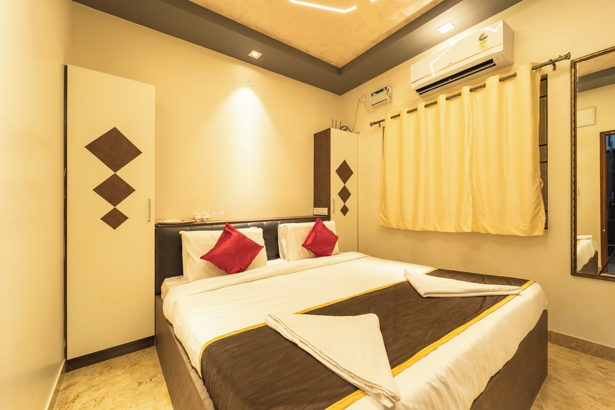 A hotel room with a bed, an air conditioning unit, a mirror, and a curtain.