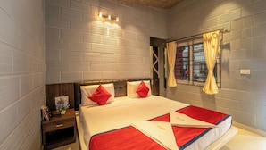 A hotel room with a large bed, a nightstand, a window with curtains, and a brick-patterned wall. - Seasons Suites HBR (Bengaluru)