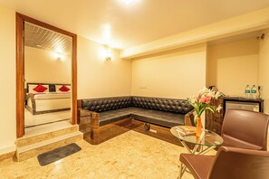 A modern living room with a sectional sofa, a glass coffee table, and a brown leather armchair. - Seasons Suites HBR (Bengaluru)