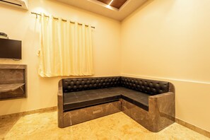 A corner seating area with a black cushioned bench, a television mounted on the wall, and a curtain. - Seasons Suites HBR (Bengaluru)