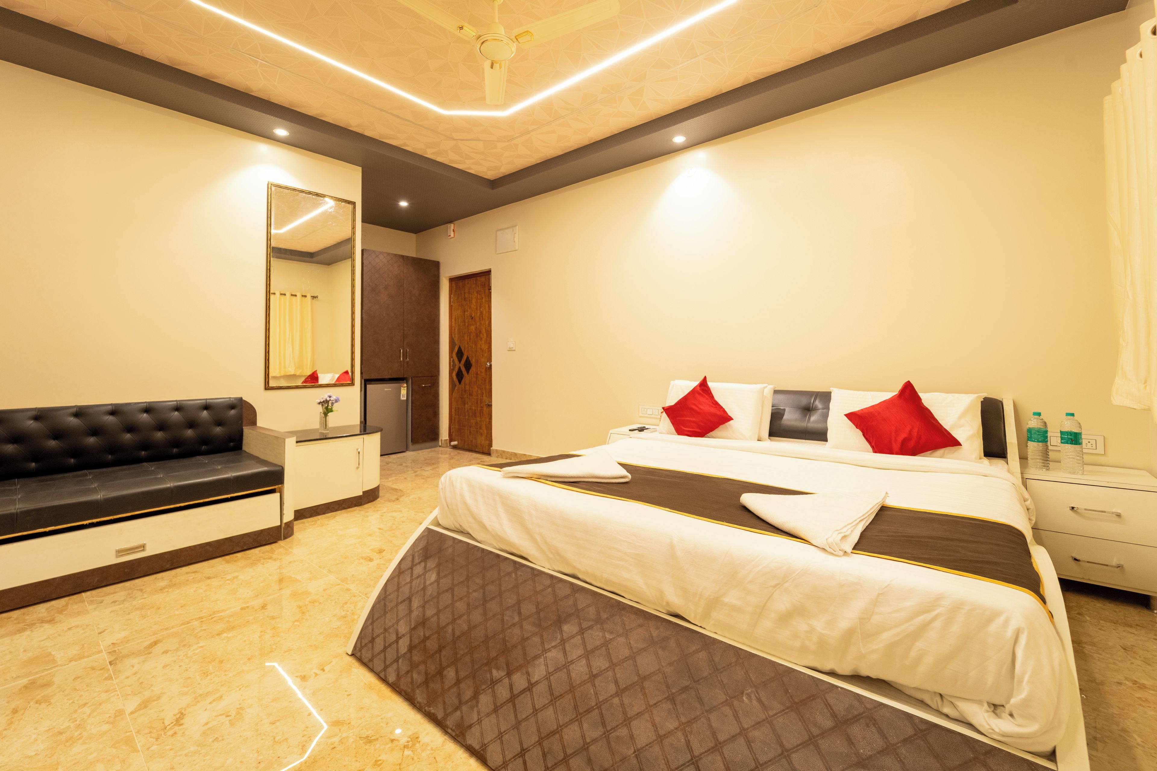 A hotel room with a bed, a sofa, a mirror, a wardrobe, and a bathroom.