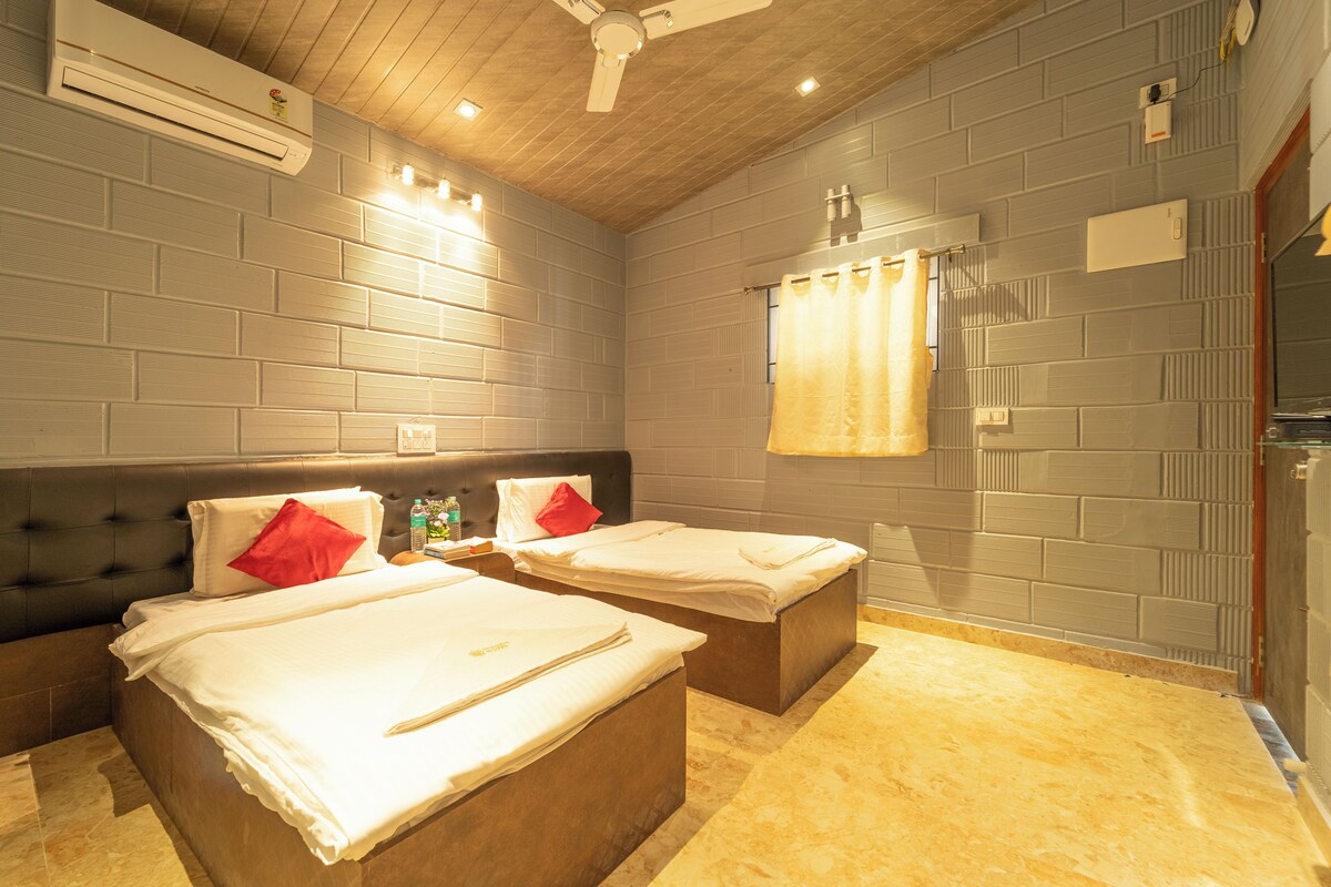 A hotel room with two beds, a wooden ceiling, and a brick wall.