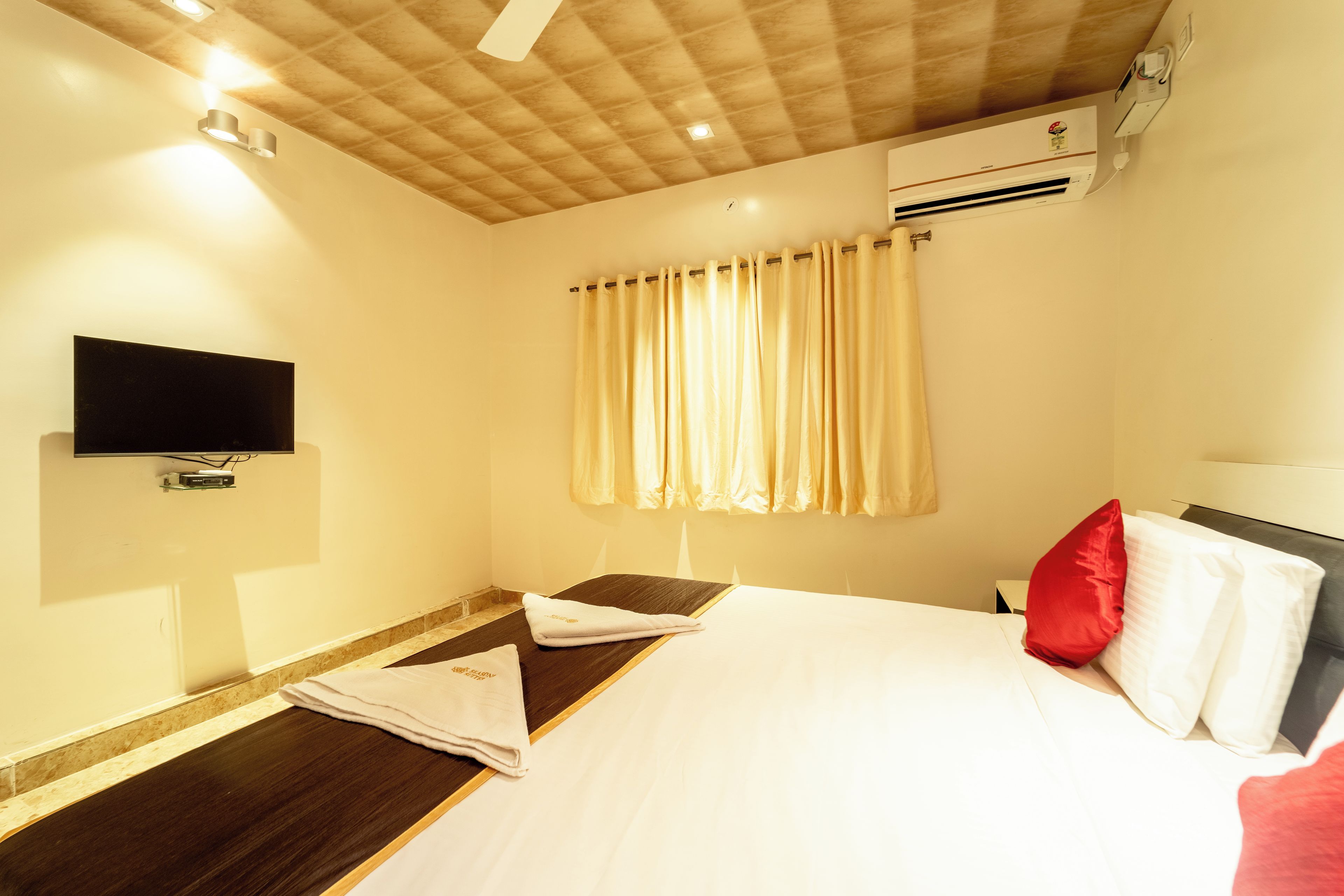 Une chambre d’hôtel équipée d’un lit, d’un téléviseur à écran plat fixé au mur, d’une fenêtre avec des rideaux et d’un appareil de climatisation.