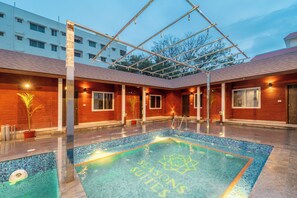 A swimming pool with a geometric pattern on the floor, surrounded by a covered area with a metal framework. - Seasons Suites HBR (Bengaluru)