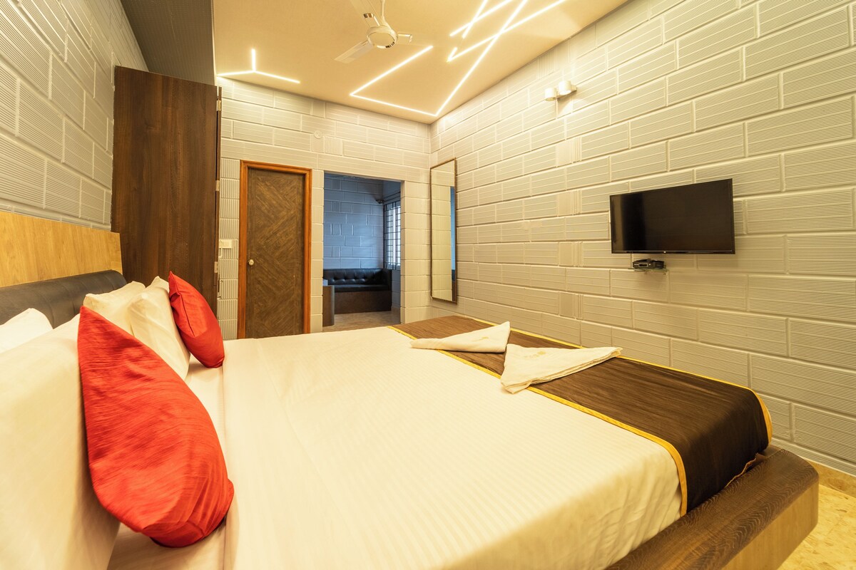 A modern hotel room with a large bed, a television mounted on the wall, and a wooden headboard.