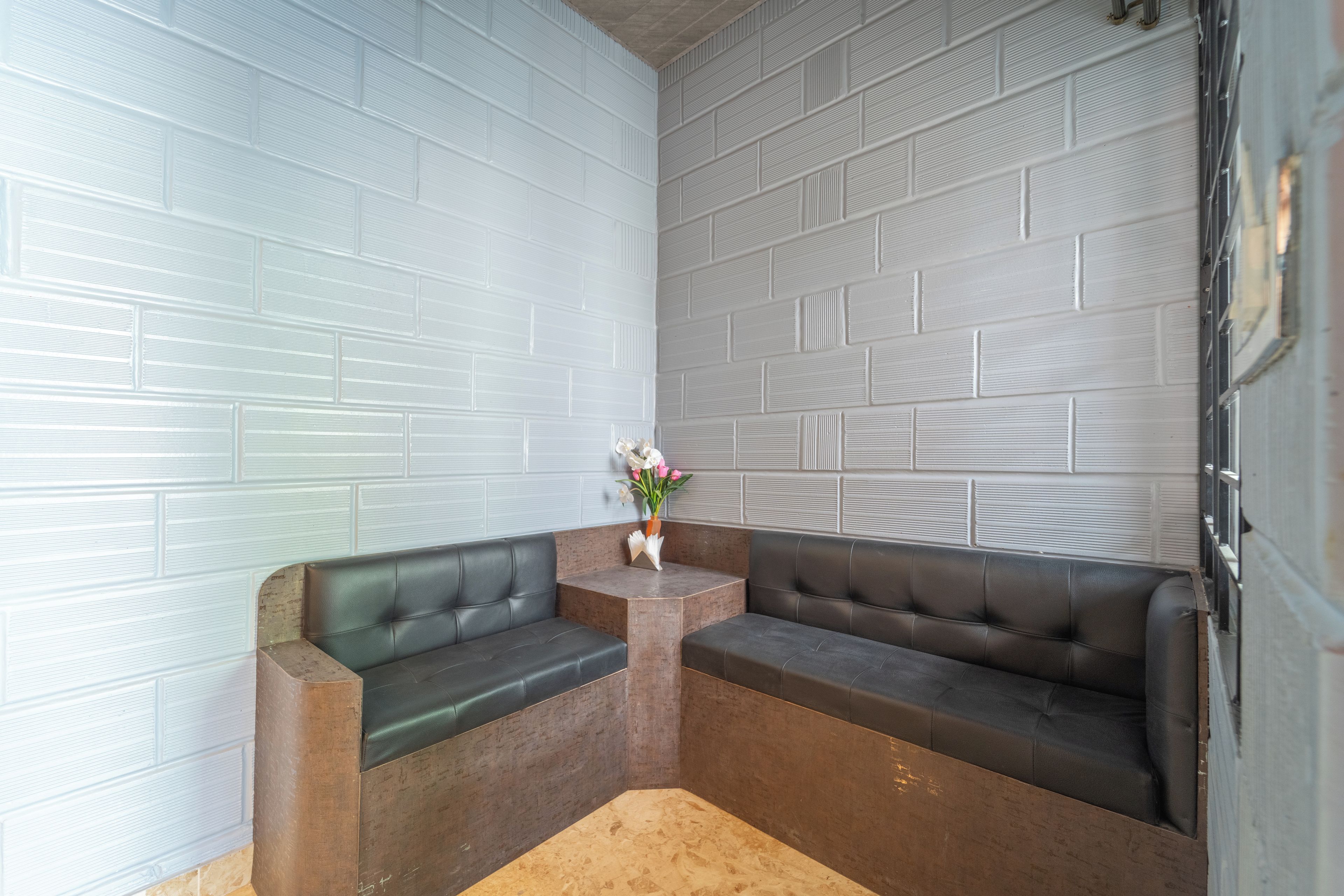 Un coin salon avec deux canapés en cuir noir, une petite table en bois ornée d’un vase de fleurs et un mur en briques blanches.