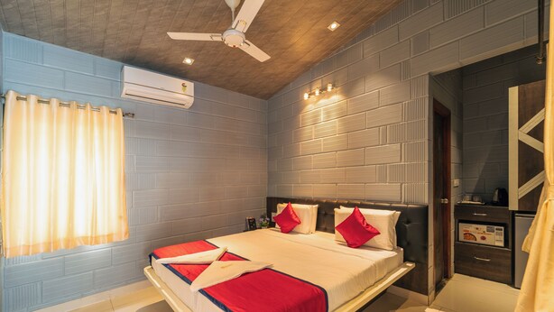 A hotel room with a large bed, a ceiling fan, an air conditioning unit, and a small kitchenette. - Seasons Suites HBR (Bengaluru)