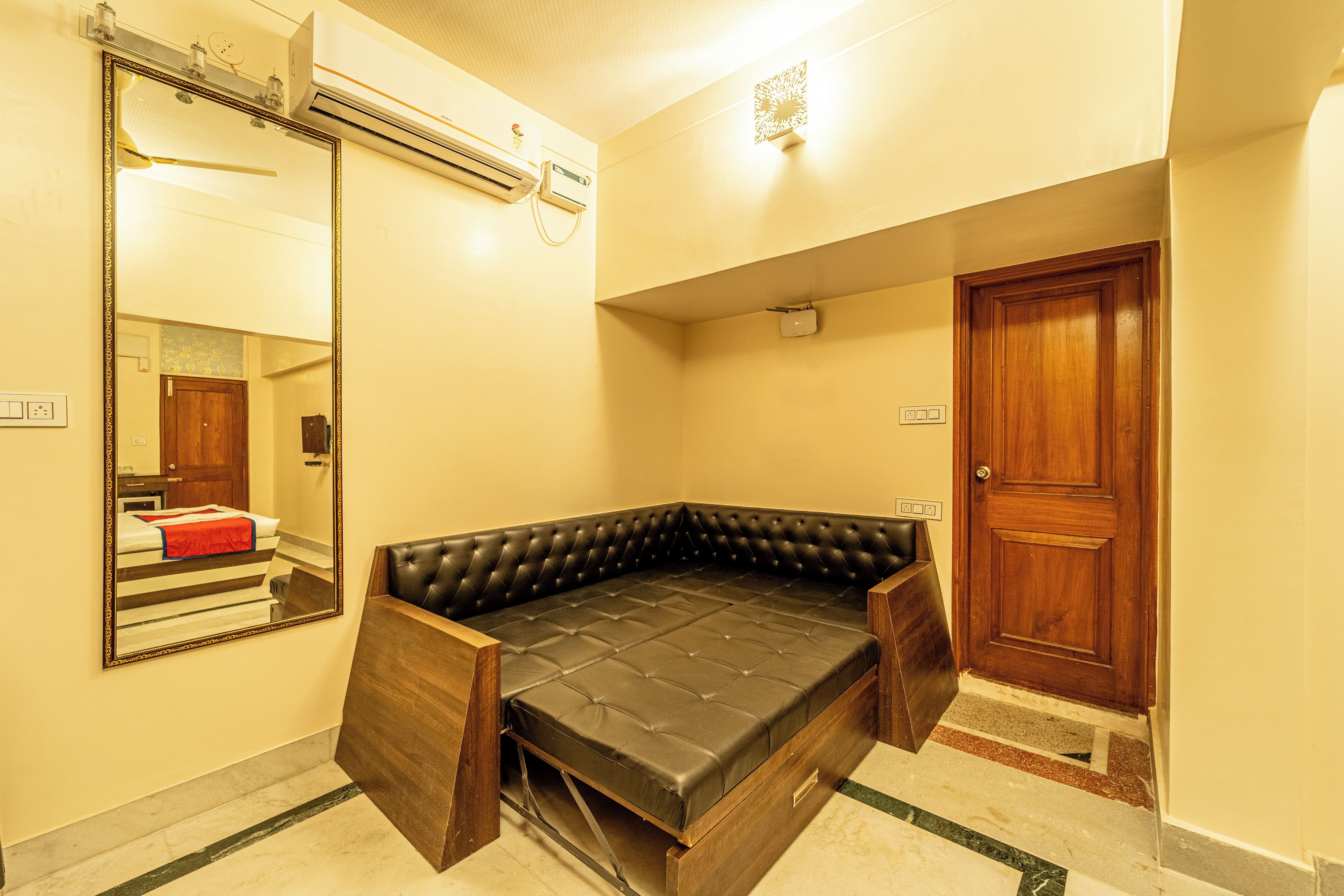 A room with a built-in sofa bed, a mirror, an air conditioning unit, and a wooden door.