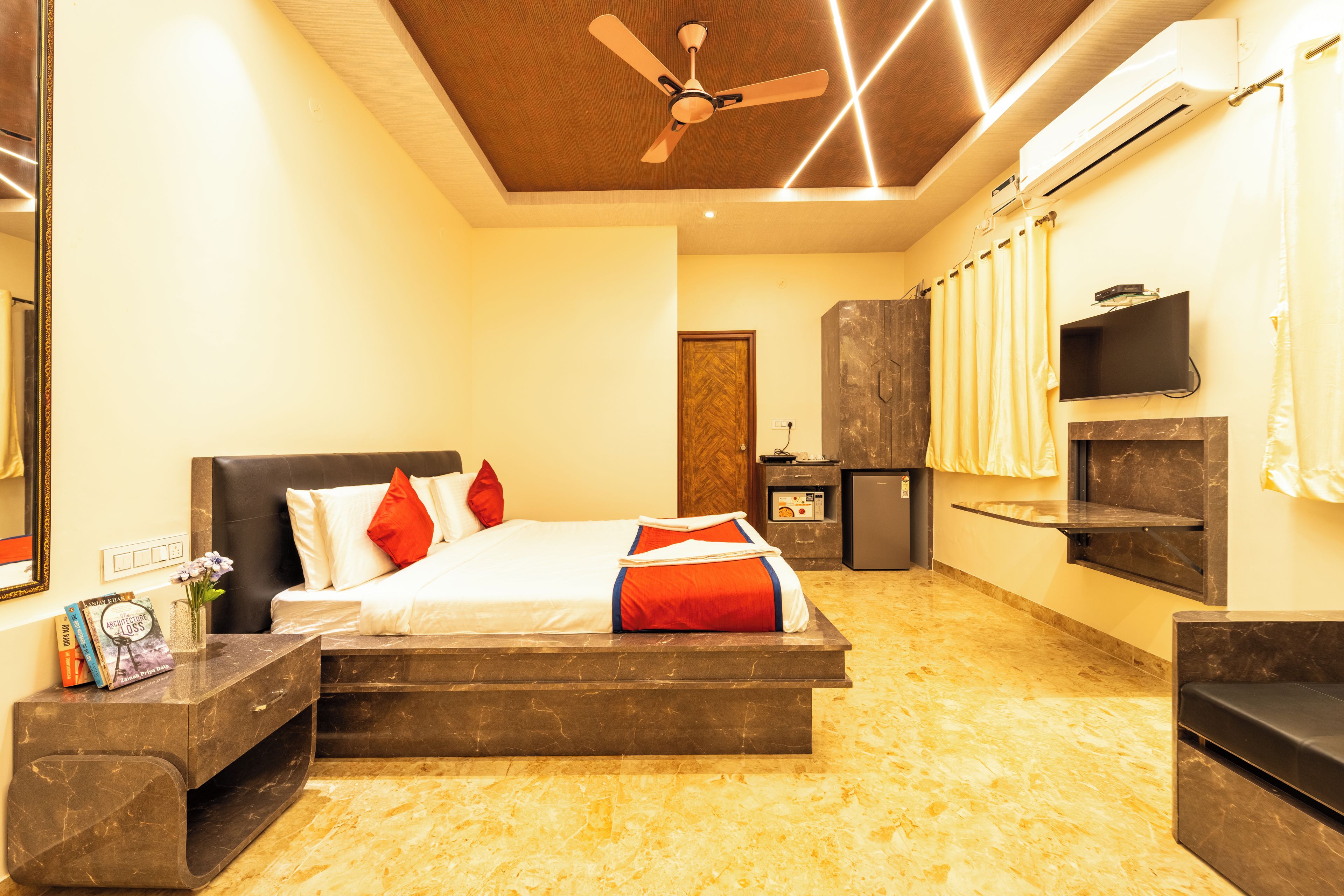 A modern hotel room with a bed, bedside tables, a TV, and a ceiling fan.