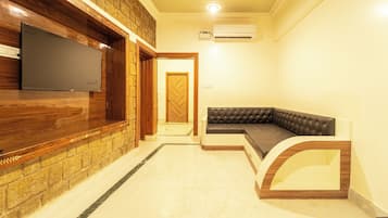 Una sala de estar con un televisor de pantalla plana montado en una pared de madera, un sofá de cuero negro y suelo de baldosas.