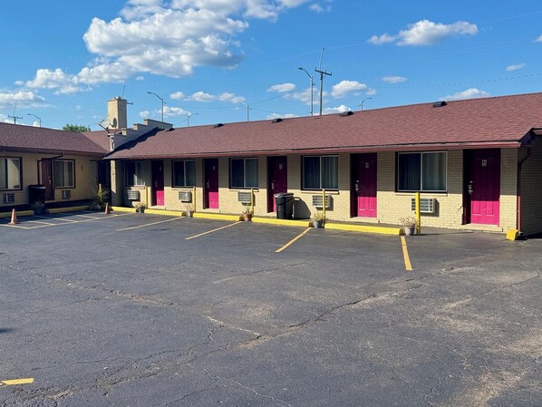 Ein Motel mit nummerierten Zimmern, einem Parkplatz und blauem Himmel.