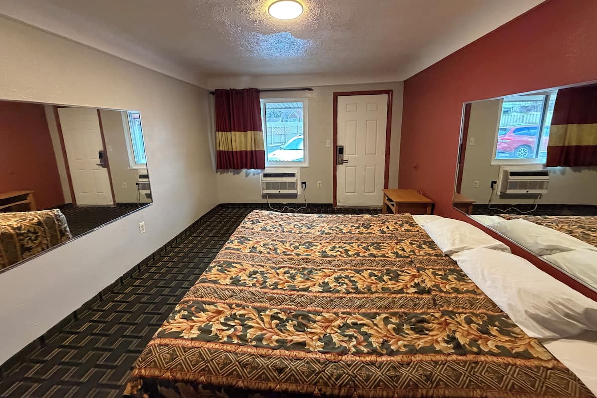 A hotel room with a large bed, two windows with curtains, an air conditioning unit, and a small table.