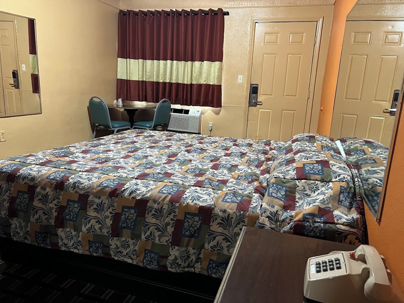 Een hotelkamer met een bed, een bureau, twee stoelen, een telefoon en een raam met gordijnen.