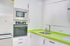 A kitchen with white cabinets, a microwave, an oven, and a sink with a green countertop. - Apartamento Celeste. (Conil de la Frontera)