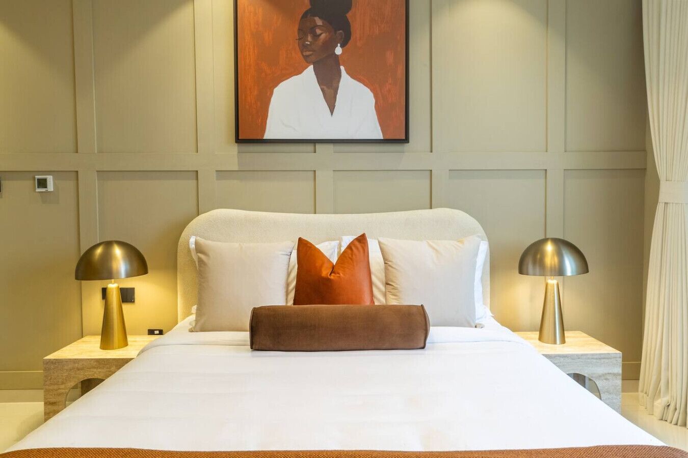 A neatly made bed with white and orange pillows, two bedside lamps, and a framed artwork above the bed.