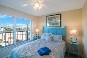 A bedroom with a large window, a ceiling fan, and a bed with matching nightstands.
