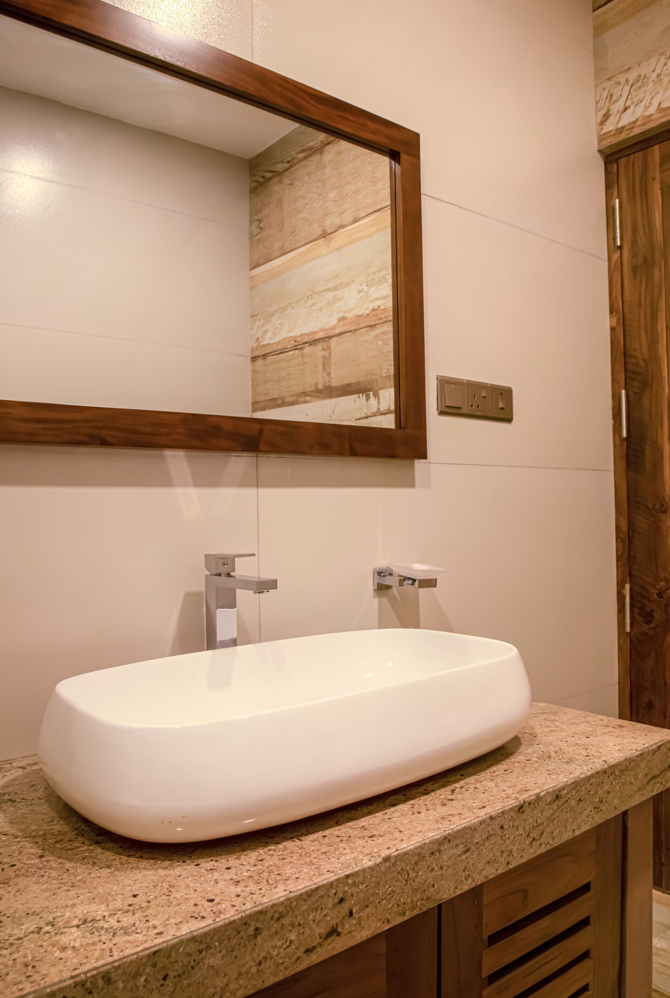 A bathroom with a white sink, a wooden-framed mirror, and a granite countertop.