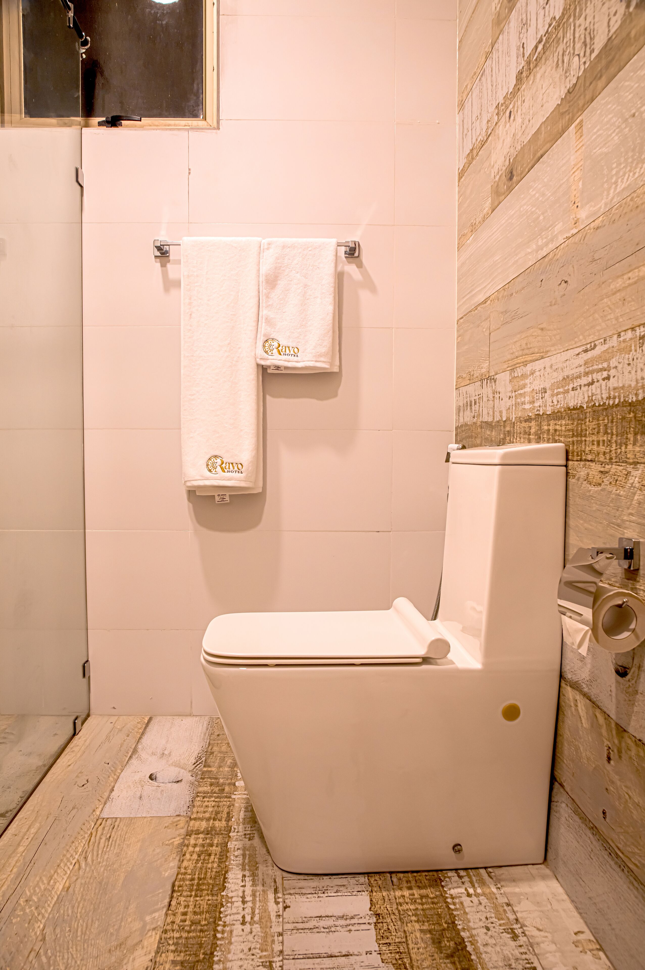 A bathroom with a white toilet, a towel hanging on a metal rack, and a wooden textured wall.