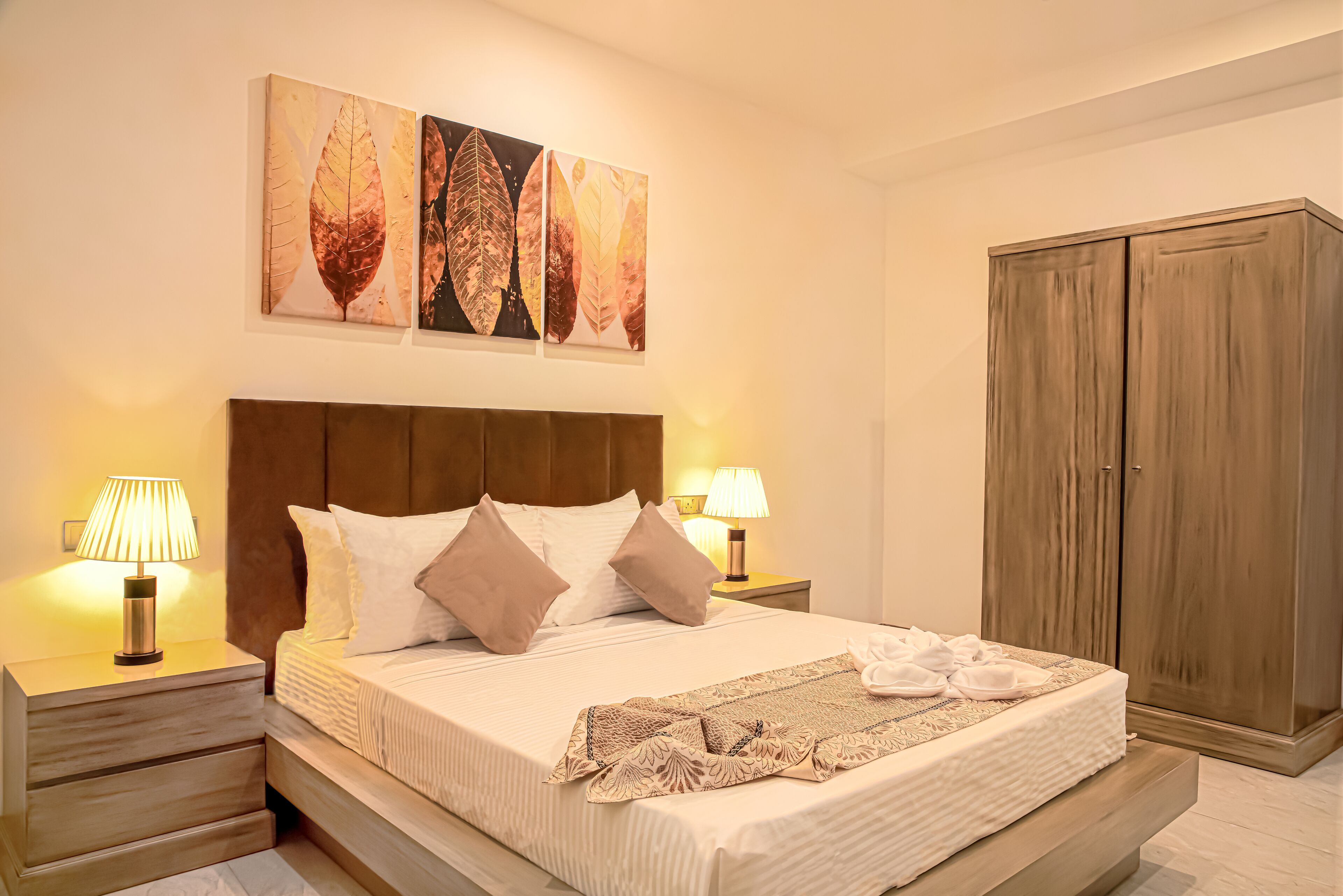 A neatly made bed with a headboard, two bedside lamps, and a large wardrobe.